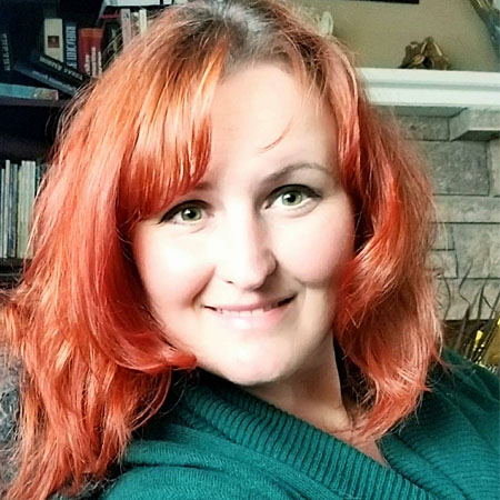 Woman with red hair and green top smiling inside.